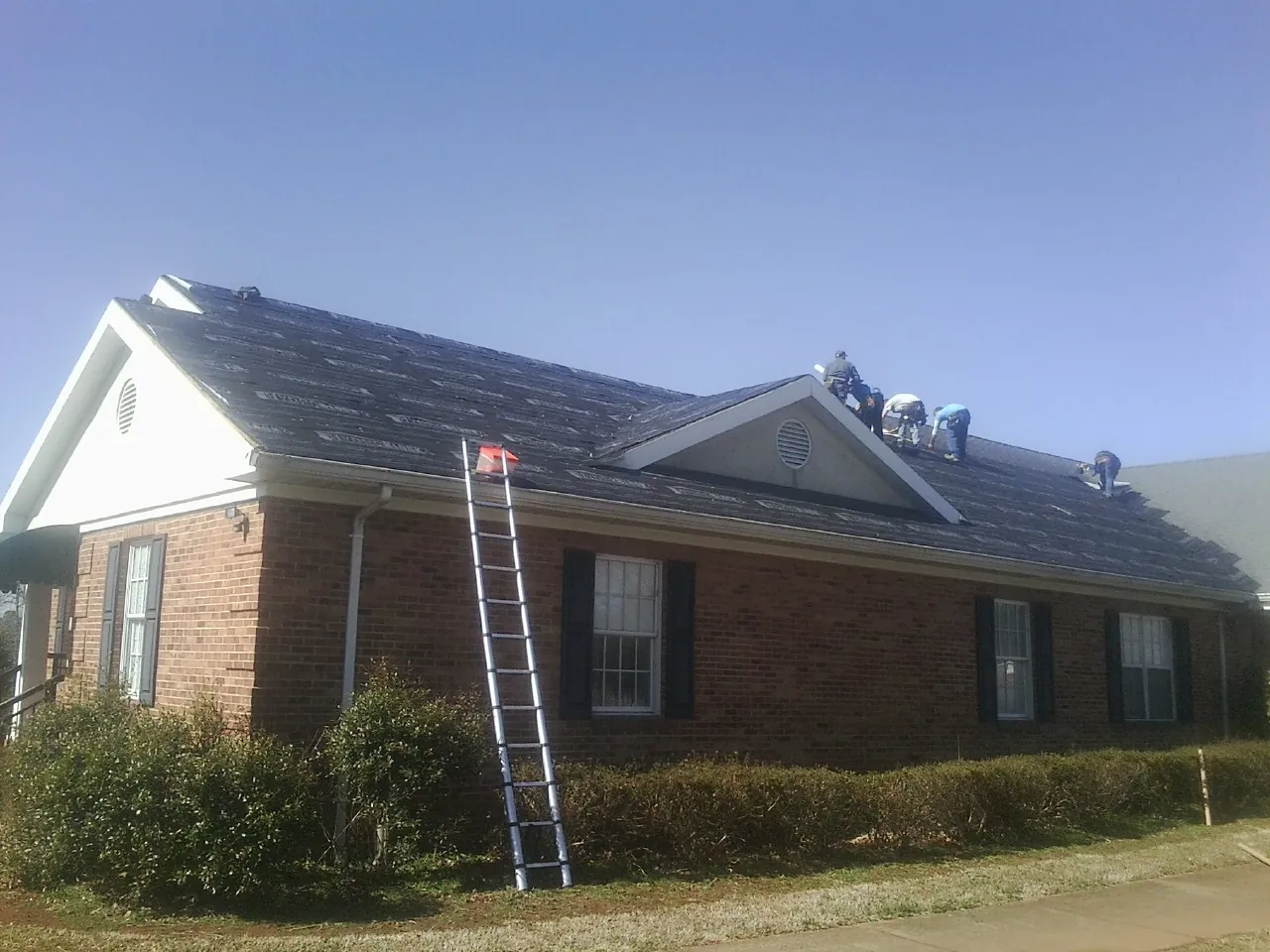 Crew tearing shingles off a brick ranch roof with a ladder set — Metal Roof Repair work by our crew in Southport