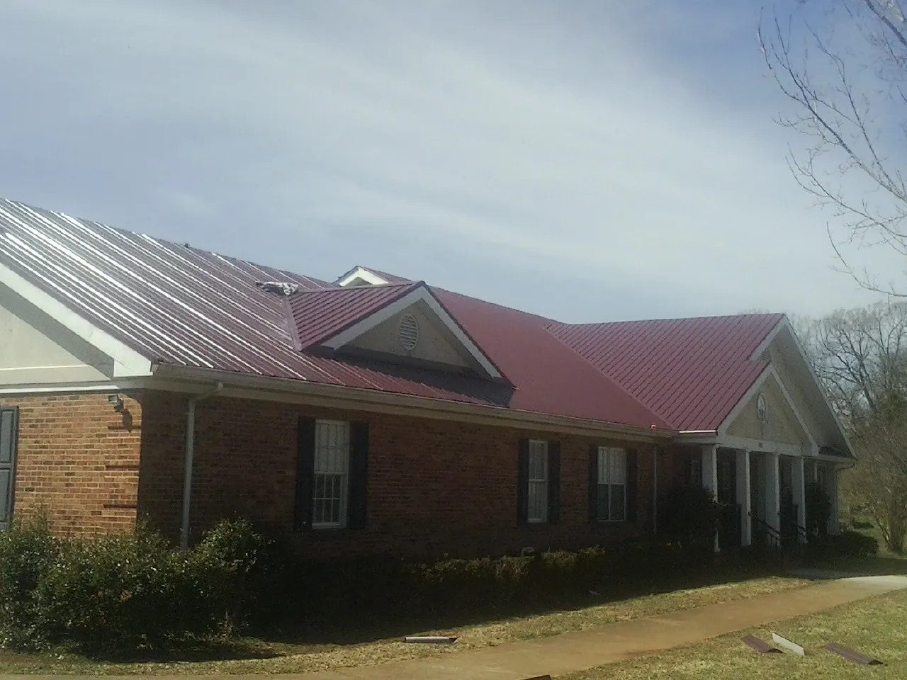 Red metal roof with gabled entries on a long brick building, from a Hail Damage Roof Repair job in Southport