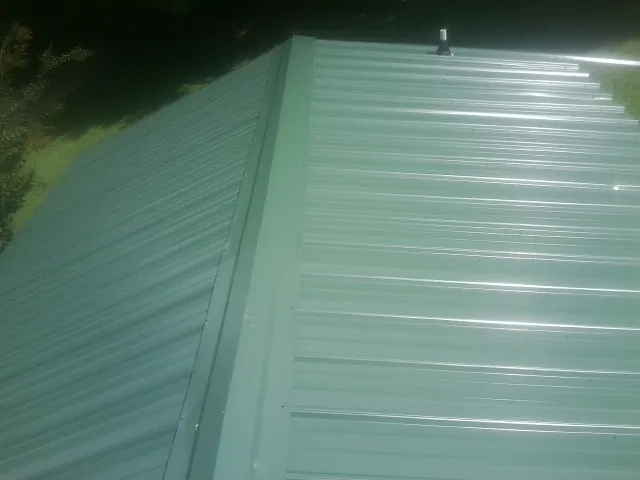 New green metal panels meeting at the ridge of a roof — Flat Roof Repair work by our crew in Southport