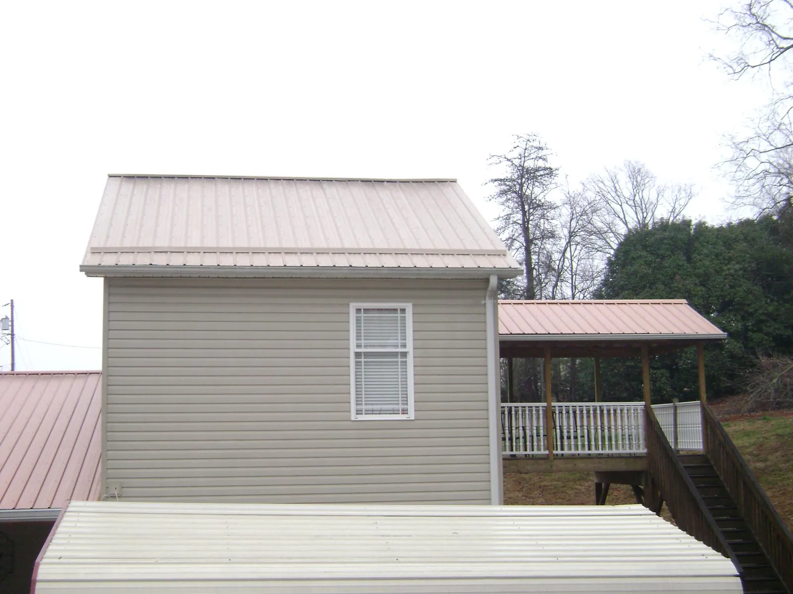 Tan metal roofs on a two story addition and attached porch, from a Roof Replacement job in Southport